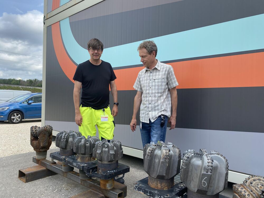 Peter Meier (CEO von Geo-Energie Suisse AG) und Olivier Zingg (Direktor der Geo-Energie Jura SA) mit verwendeten Bohrmeisseln neben dem Besucherpavillon. (Foto: Mathias Küng)
